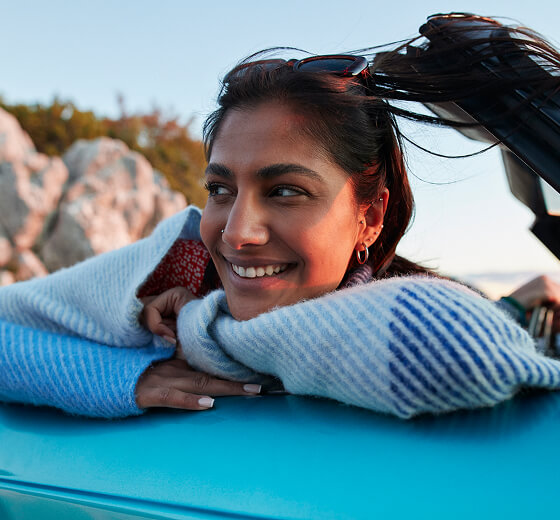 person leaning on car with hands folded under chin